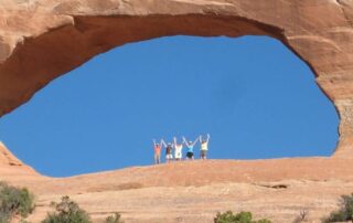 Small group of women posing in the distance beneath massive red rock arch