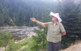 Woman in paper hat gesturing to the woods of Idaho