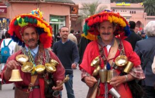 Moroccan locals in colorful clothing with gold tins hanging from their necks