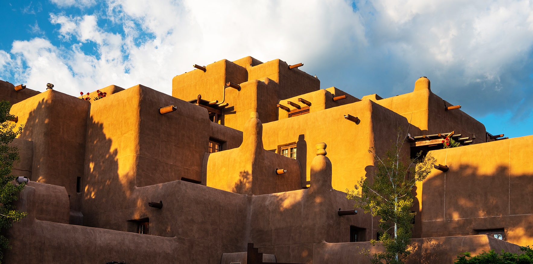 Dramatic blue sky with white storm clouds over an historic pueblo style building glowing at sunset in Santa Fe, New Mexico