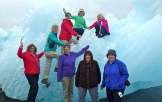 Women atop a giant piece of blue ice in Jökulsárlón Ice Lagoon, Iceland