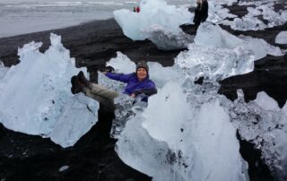 Woman sitting on large piece of ice in Jökulsárlón Glacier Lagoon: Travel to the black sand beaches of Iceland with Canyon Calling Tours for women only