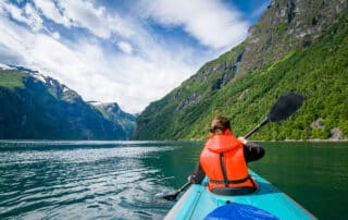 Woman kayaker in bright orange life vest on her trip in Geiranger fjord waters. Geirngerfjord, Norway.