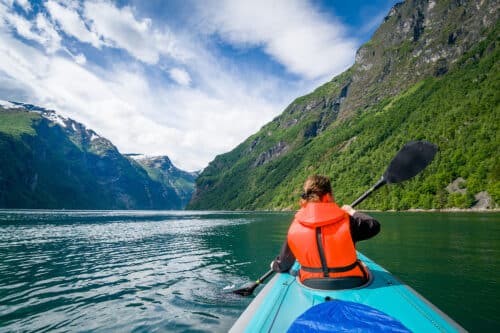 Woman kayaker in bright orange life vest on her trip in Geiranger fjord waters. Geirngerfjord, Norway.