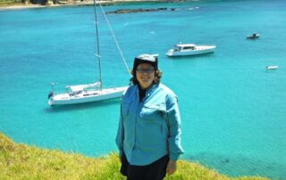 Woman posing above expanse of turquoise sea speckled with boats: Hiking trips to New Zealand